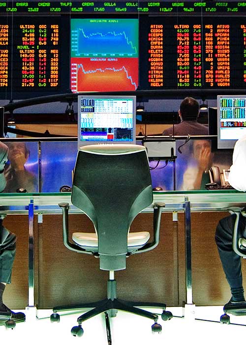 Two stock market traders reflected in their screens, sitting in front of list of stock prices