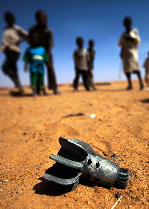 Remnant of a mortar projectile on the ground in front of a group of children in an IDP camp
