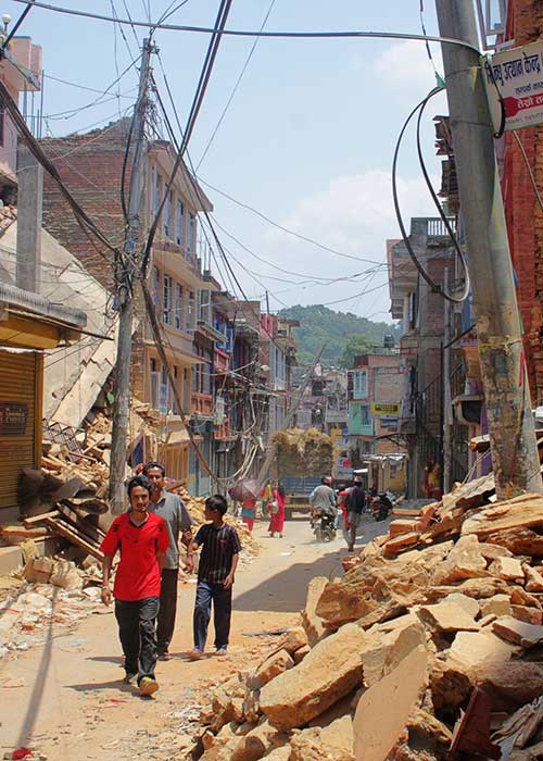 People walking down street in urban environment where several buildings have collapsed following a disaster